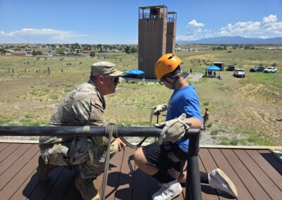 Soldier coaches a youth participant on rappelling technique atop a training tower