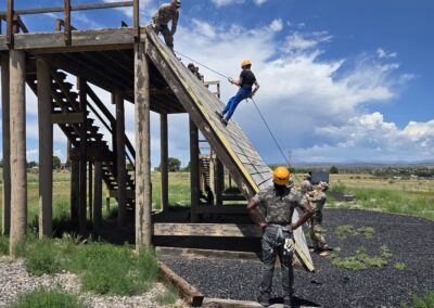 Youth participants rappel down an outdoor training structure supervised by soldiers