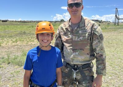 A soldier poses with a youth participant wearing a climbing helmet and rappelling harness during a Guard family event