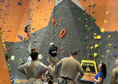 Youth and soldiers participate in an indoor rock climbing activity at a climbing gym