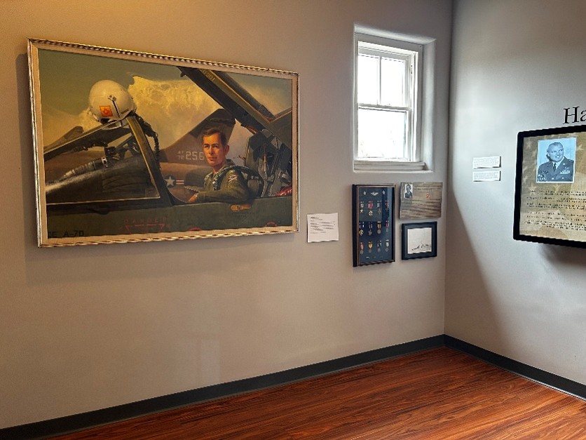 Museum gallery displaying a military pilot painting, framed medals and historical documents
